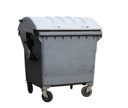 A large, grey plastic rubbish wheelie bin with a hinged lid, situated outdoors on a paved surface. The bin features a textured surface with ridges along the lid and body, and is equipped with four small black wheels at the base for mobility. It is positioned in a driveway or pathway, with a background that suggests an urban or suburban setting, possibly near residential buildings or commercial premises in Osterley. The bin's side handles are visible, and the environment appears well-lit, indicating daytime. This image relates to waste management services provided by Commercial Waste Osterley, focusing on rubbish collection and disposal for local businesses or residents in the Osterley area, underscoring the importance of organized waste removal.